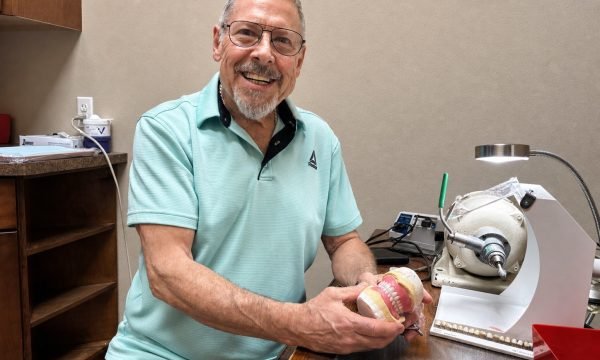 Star Dental's on-site denture technician holding a denture model beside laboratory equipment